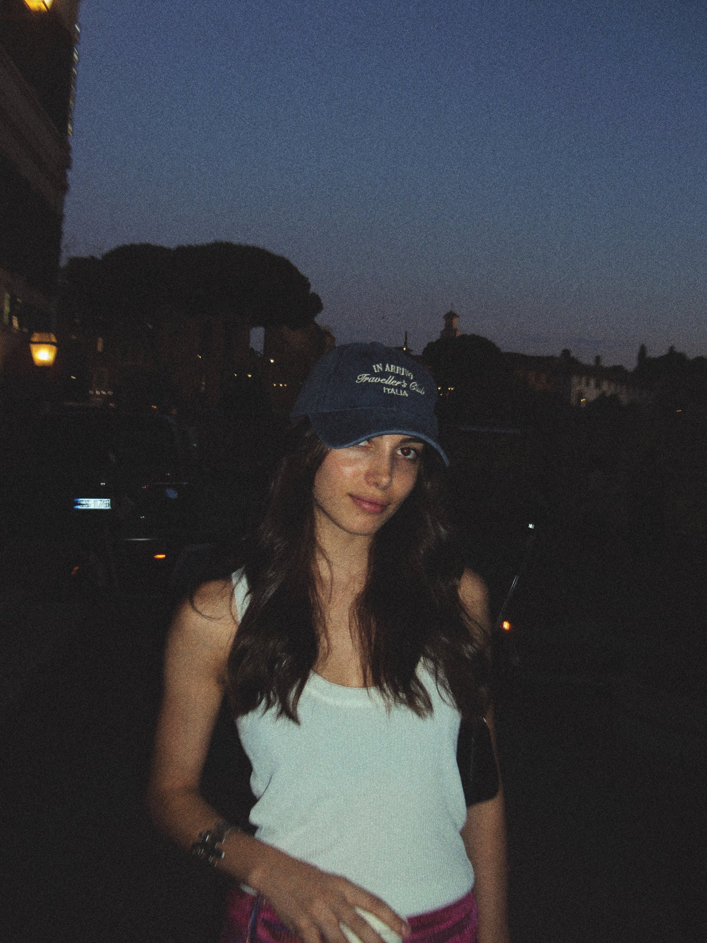Woman wearing a blue cap and white tank top at night with blurred background in arrivo italian lifestyle brand