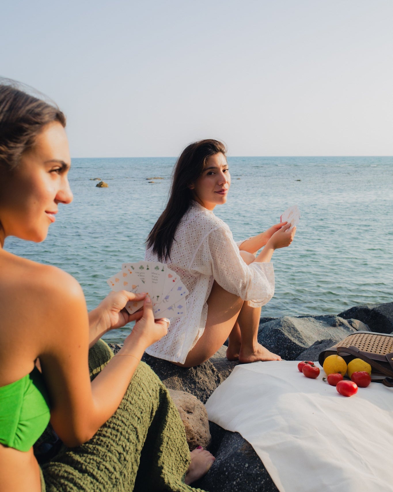 Two women playing cards by the ocean having a picnic.