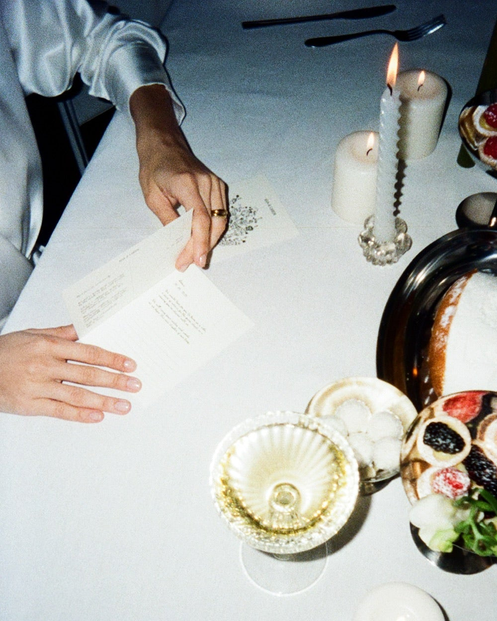 Two views of a table setting with candles and decorative items, one showing hands holding a piece of paper.