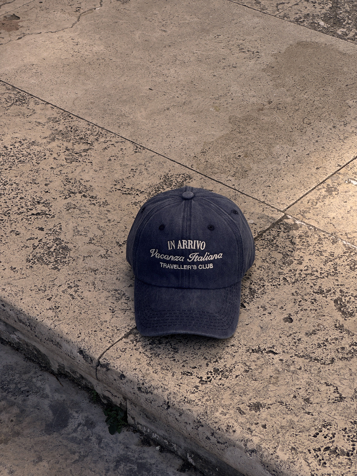 Navy blue cap with white text on a concrete surface in arrivo italian lifestyle brand